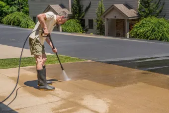 A man is using a high pressure washer to clean a sidewalk.