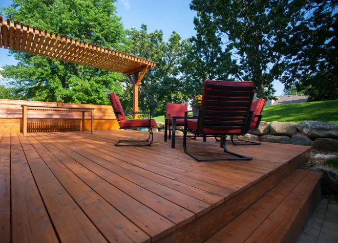 A wooden deck with chairs and a table under a pergola.