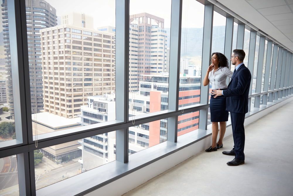 A Business Man and Woman in Suits Looking Out a Large Window at a City — Country Coast Valuers in Cundletown, NSW