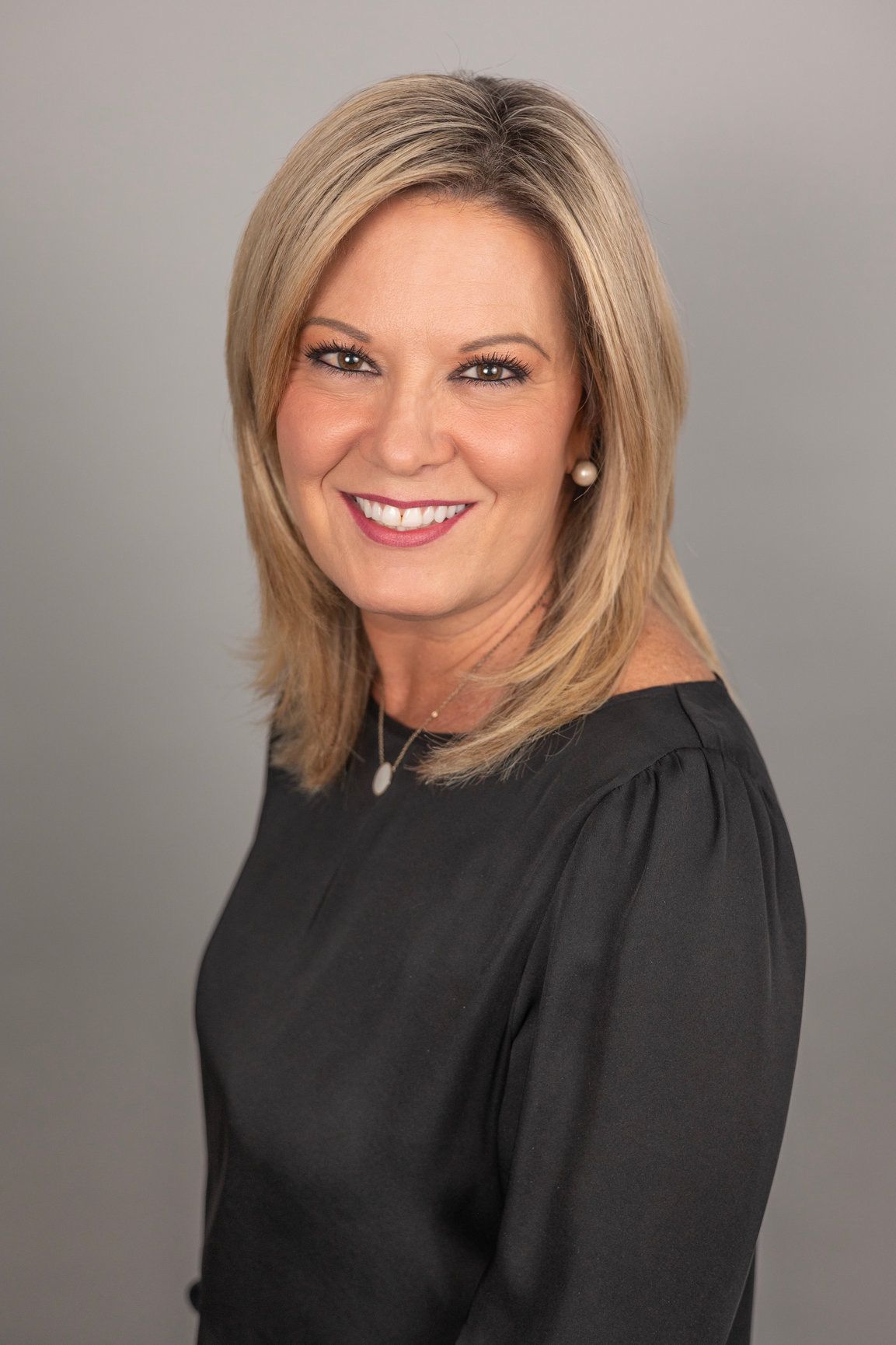 A woman wearing a black shirt and a necklace is smiling for the camera.