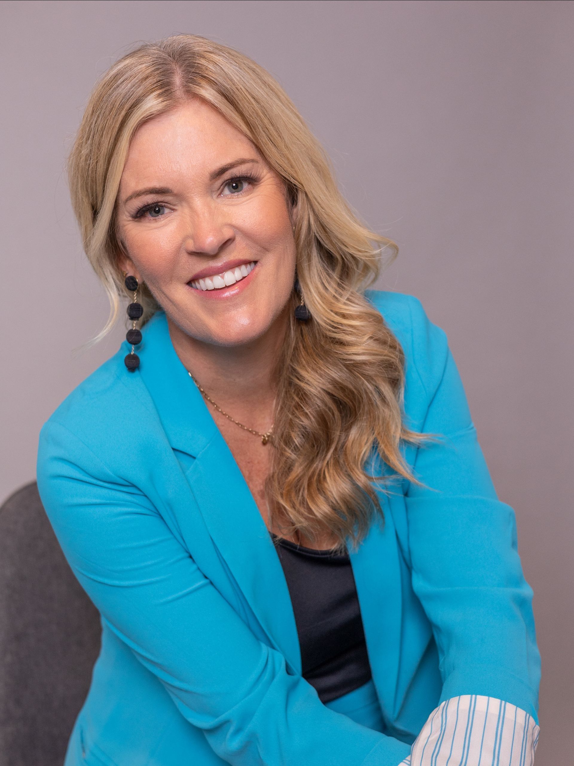A woman in a blue jacket is sitting in a chair and smiling.