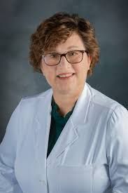 A woman in a white lab coat and glasses is smiling for the camera.
