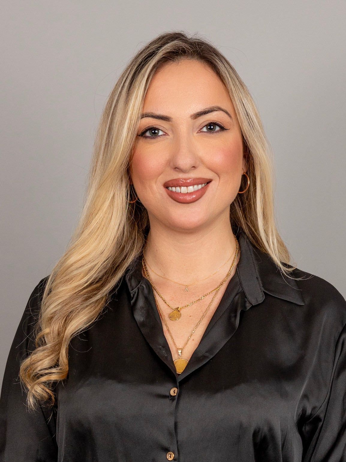 The woman is wearing a black shirt and a gold necklace.