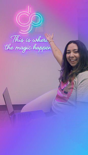 Woman smiling, pointing up toward neon sign that says 