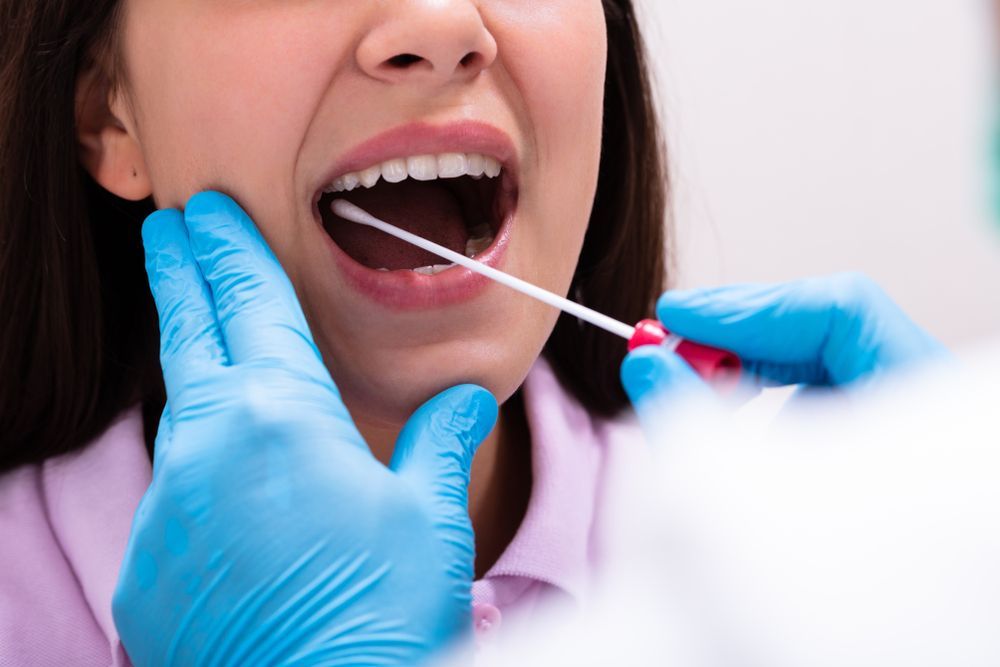 Dental exam with gloved hands swabbing the inside of a patient's open mouth
