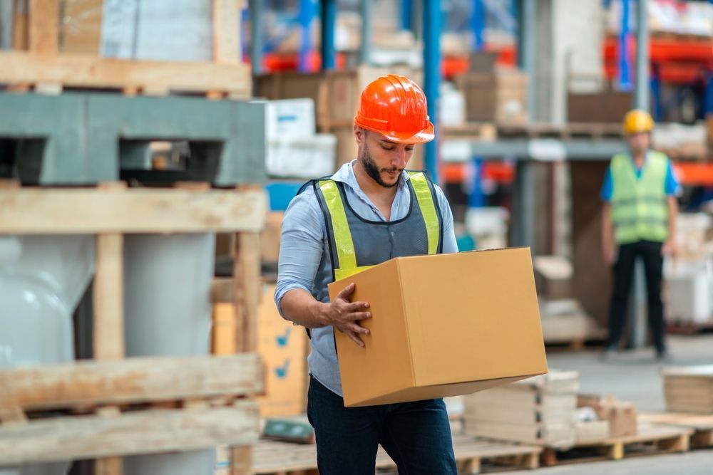 Worker in orange hard hat carrying a cardboard box at a construction site