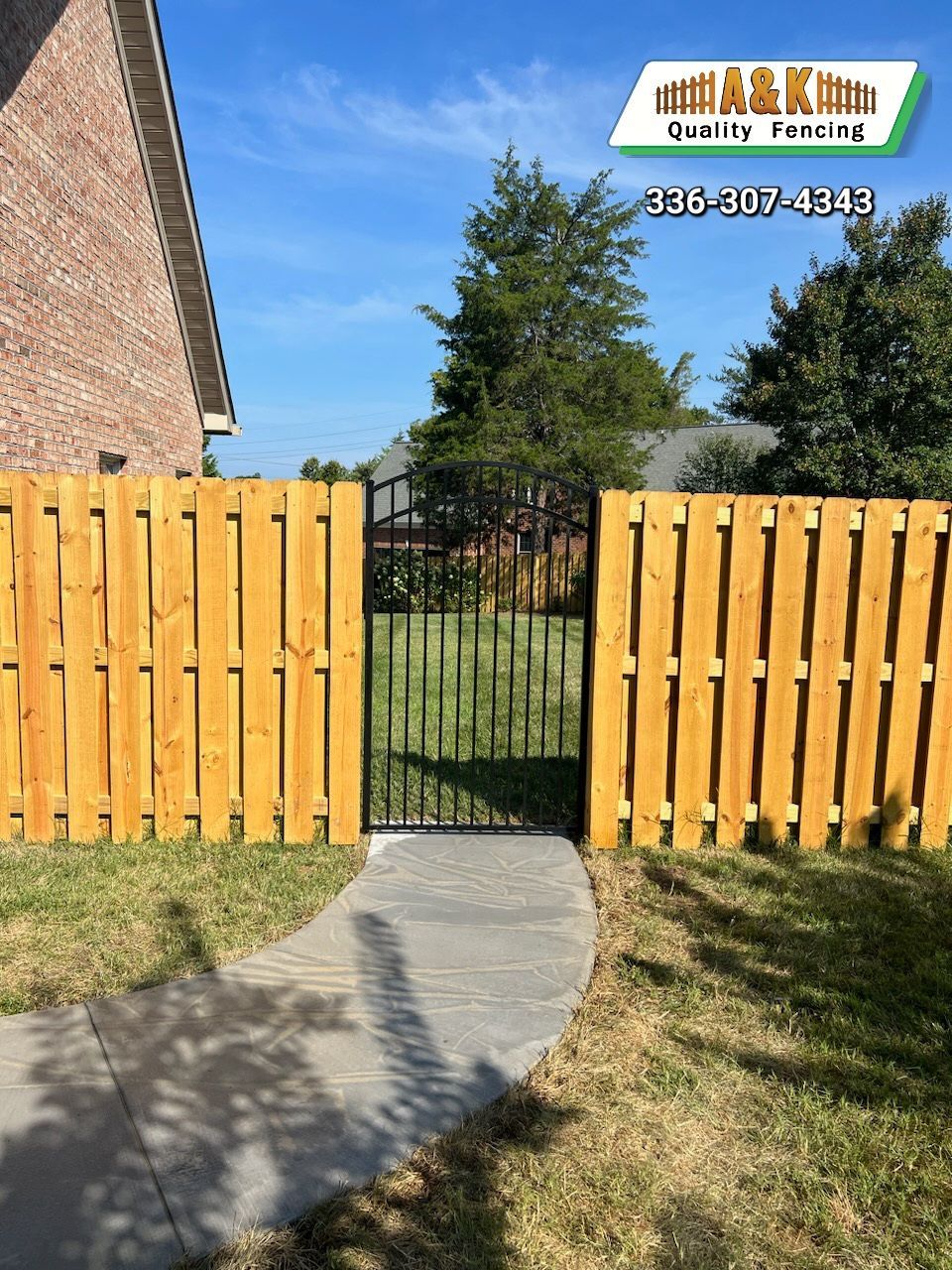 A wooden Shadow Box fence with a Aluminum gate is next to a sidewalk.