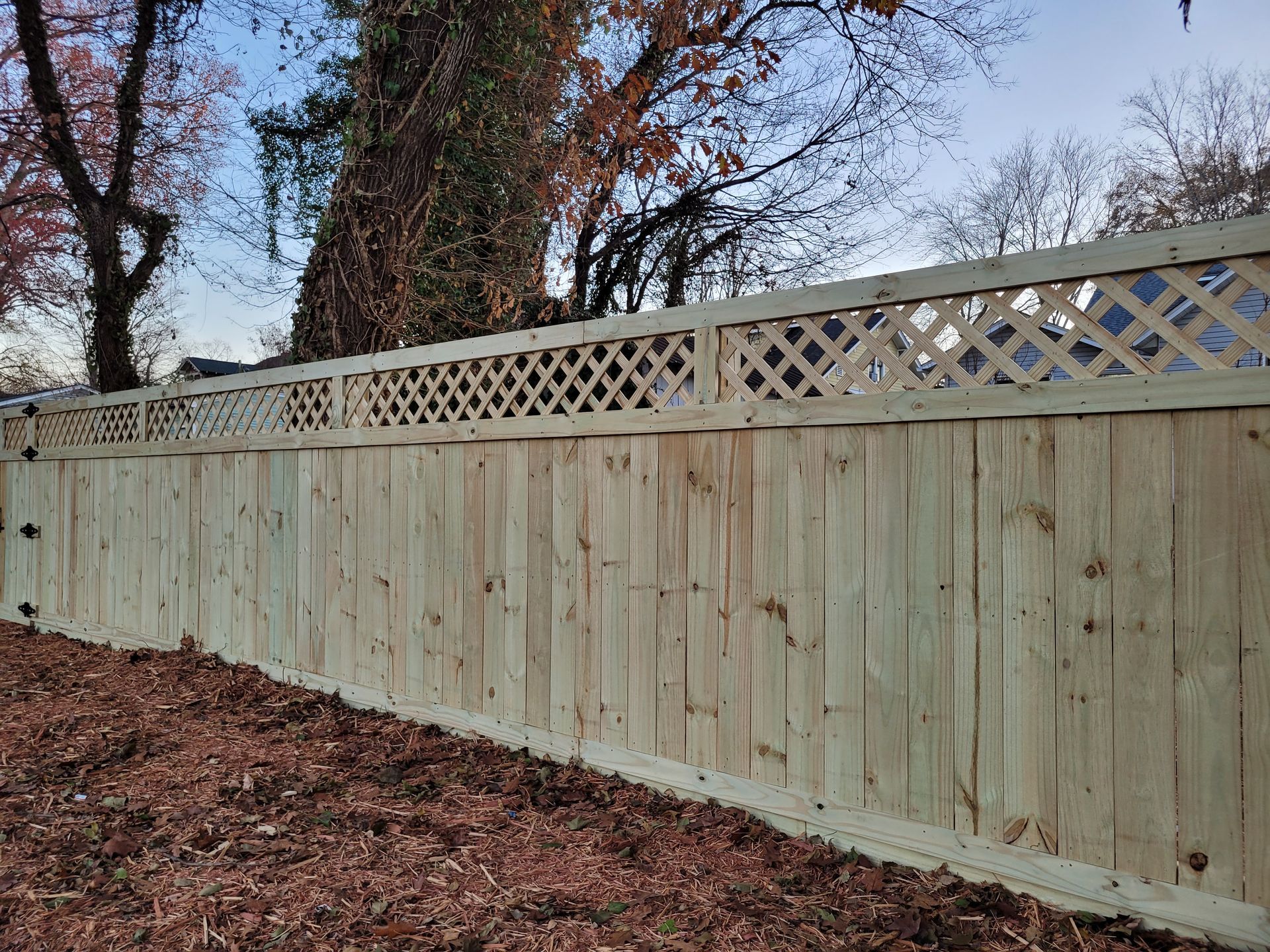 A wooden fence with a lattice top is sitting in the middle of a yard.