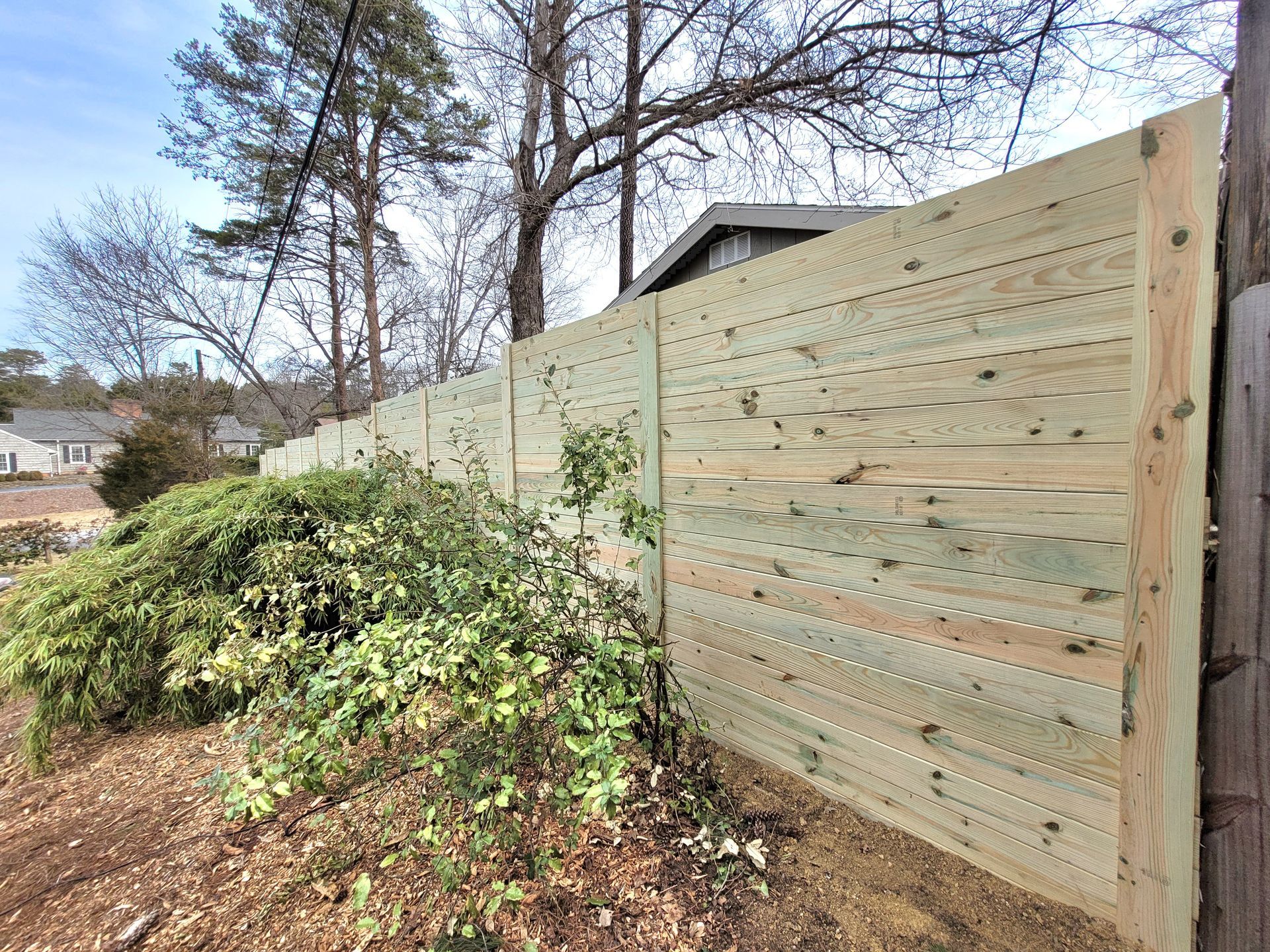 A wooden horse zone fence is surrounded by bushes and trees in a yard.