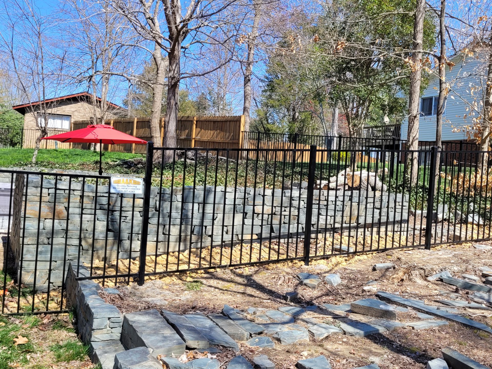 A black Aluminum fence with a red umbrella in the background.
