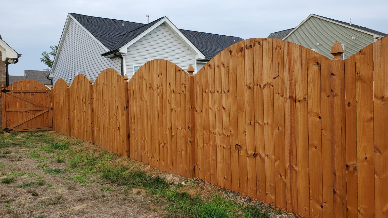 A wooden Privacy  fence with a arched design in the backyard of a house.