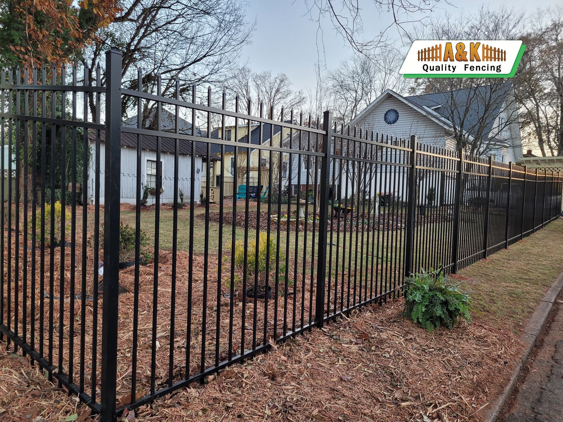 A Aluminuml fence surrounds a yard in front of a house.