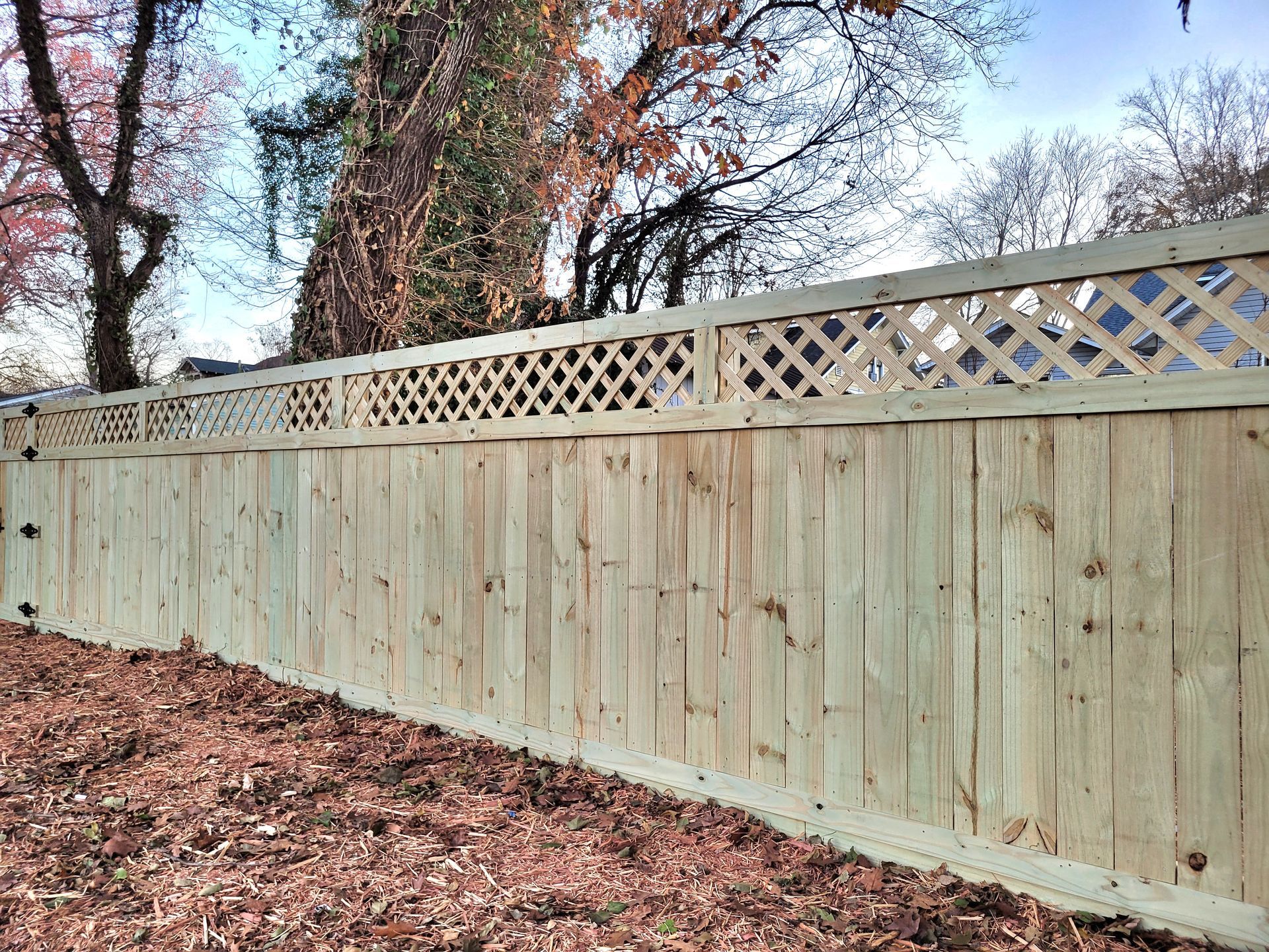 A wooden Privacy  fence with a lattice design and a tree in the background.