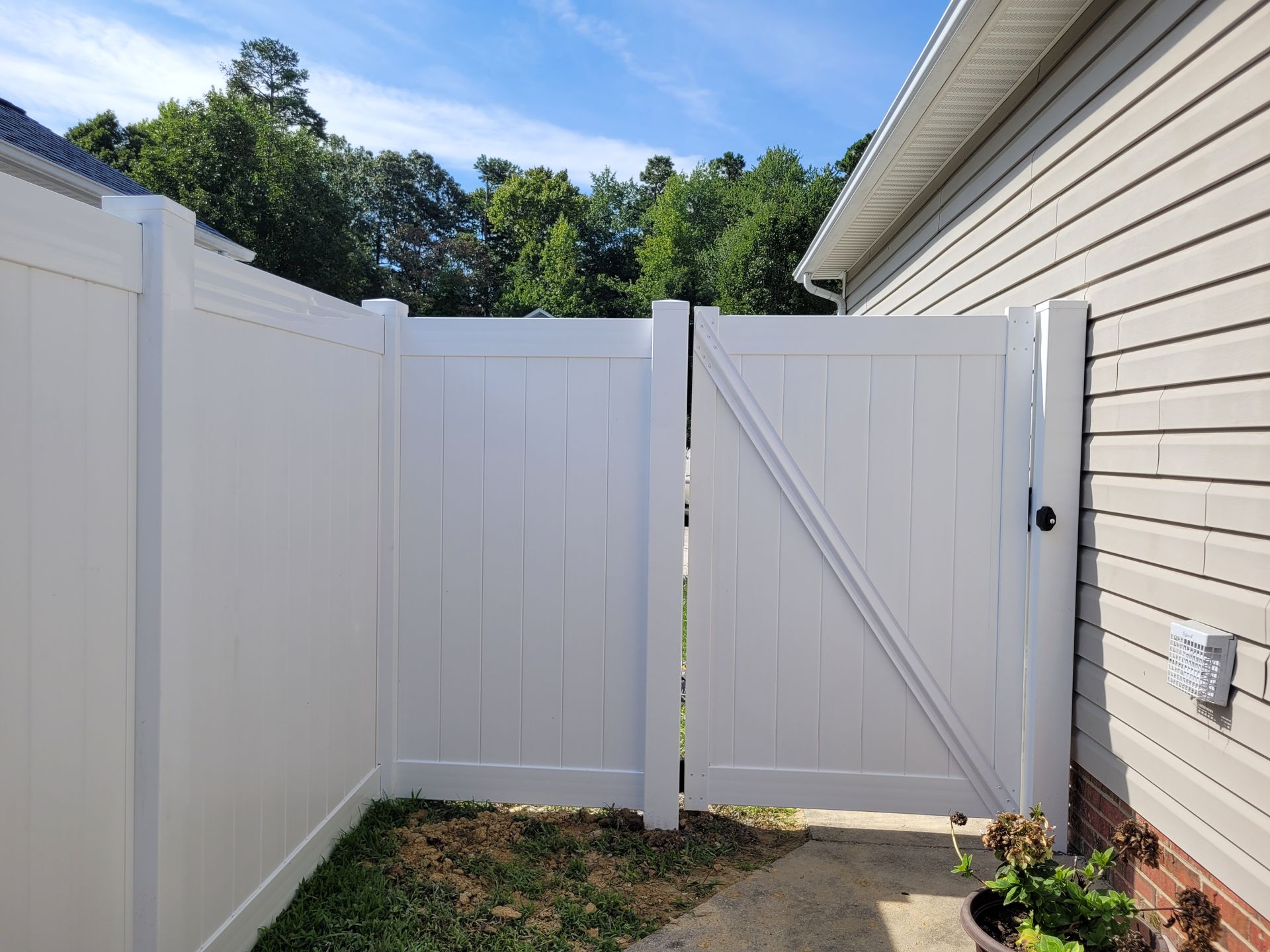 A white Vinyl fence with a gate in the backyard of a house.