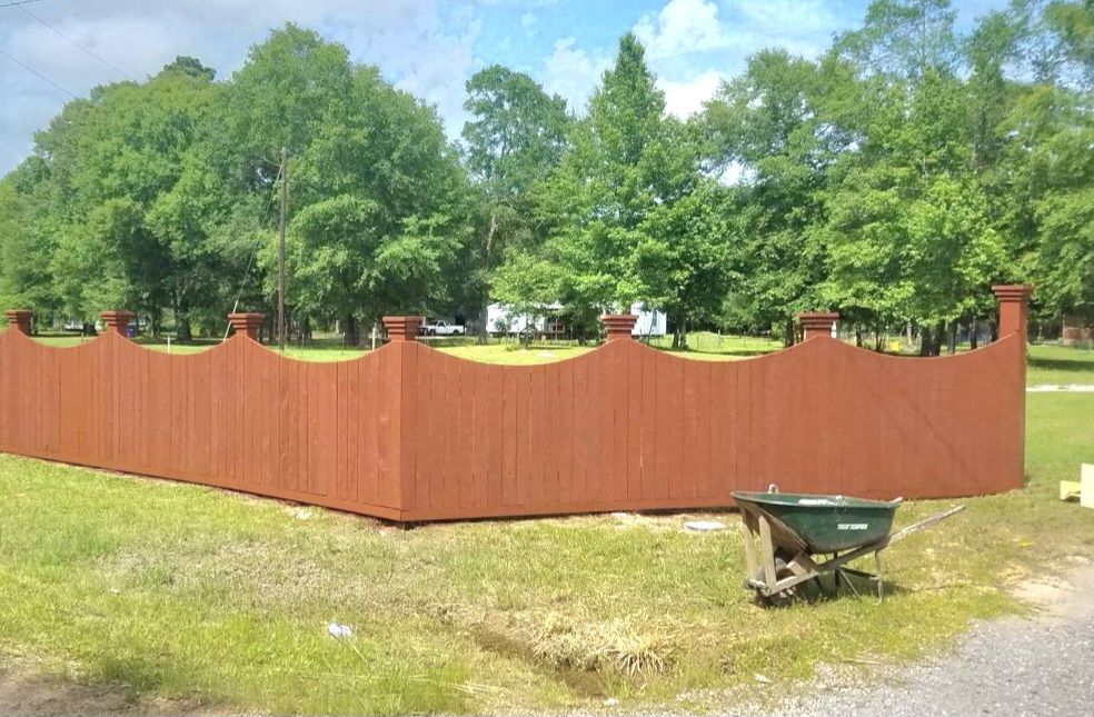 A wooden fence with a green wheelbarrow in front of it.