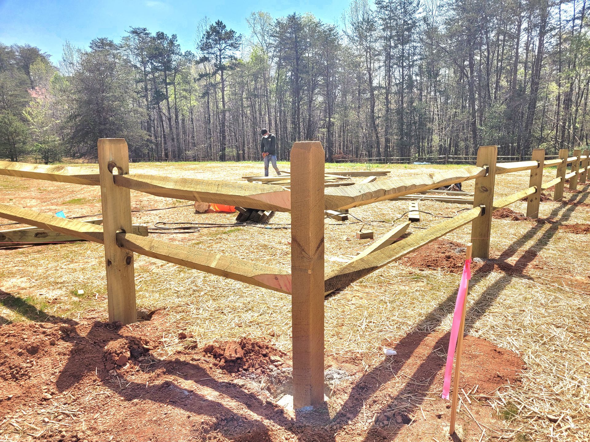 A wooden split rails fence is being built in a field with trees in the background.