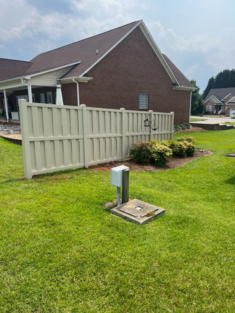 A Tan Vinyl fence surrounds a lush green lawn in front of a brick house.