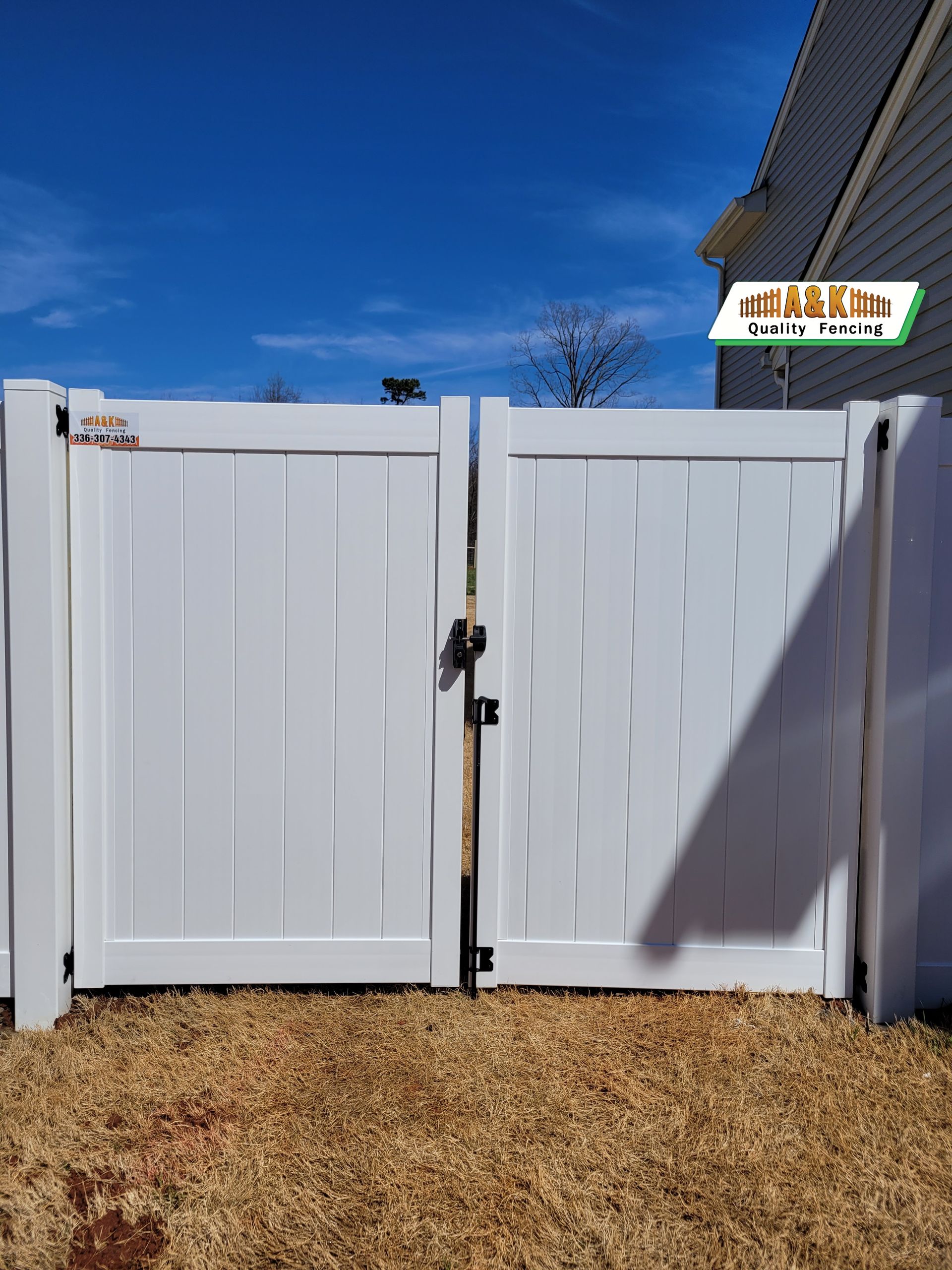 A white Vinyl fence with a gate in the backyard of a house.