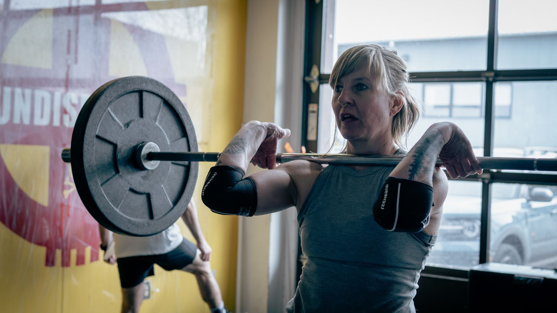 A woman is lifting a barbell over her head in a gym.