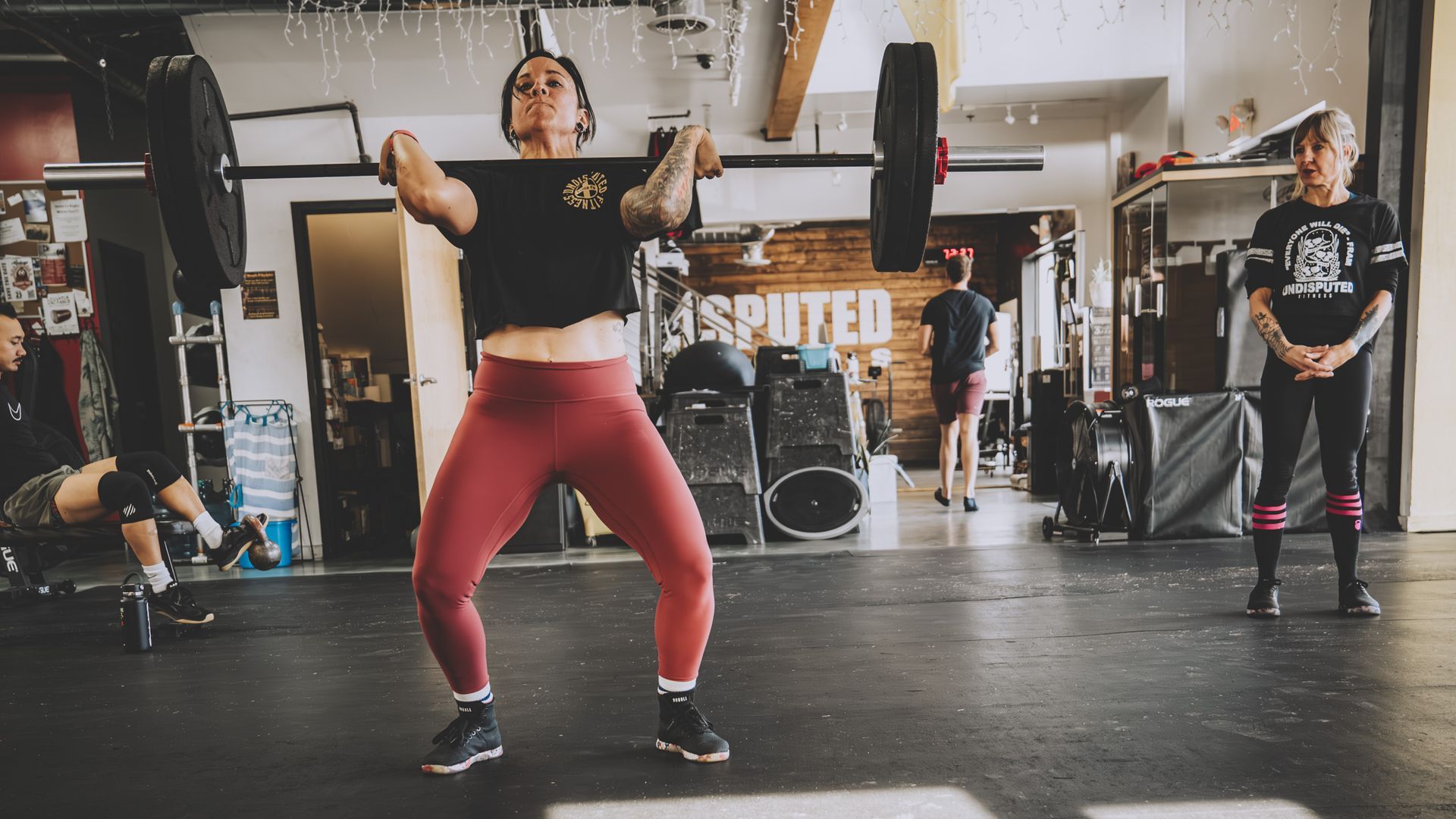 A woman is squatting with a kettlebell in a gym.
