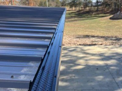 Dark metal roof with gutter guard, overlooking a concrete driveway and grassy yard.