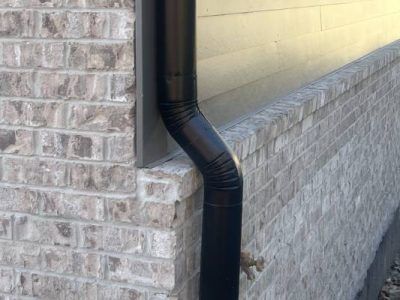 Black downspout against brick wall.
