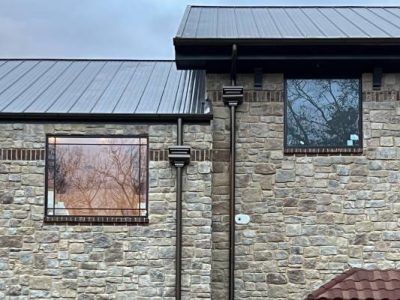 Stone building with metal roof, windows reflecting trees, and bronze-colored gutters.