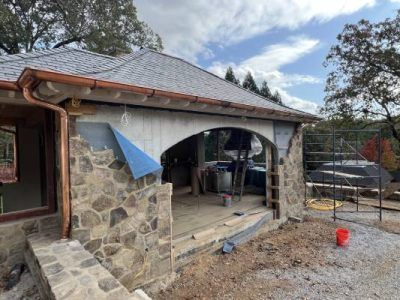 Stone building under construction with copper gutters and a blue protective sheet.