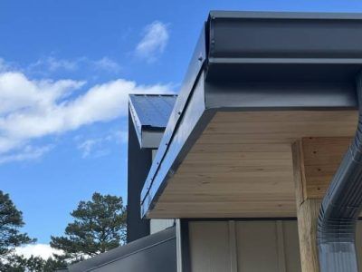 Modern house exterior with dark gray gutters and soffit against a blue sky.