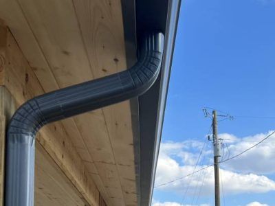 Dark gray gutter and downspout on a wooden building against a blue sky.