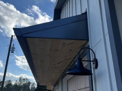 Modern, dark blue metal awning with wood underlay, mounted on a building. A black gooseneck lamp is mounted beneath.