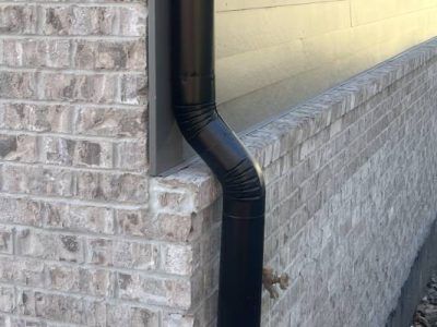 Black downspout on a brick wall, directing water away from the building.