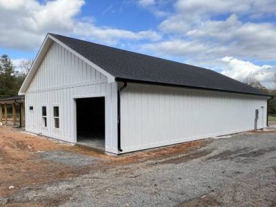 White barn-style building with a black roof and open garage door, under construction.