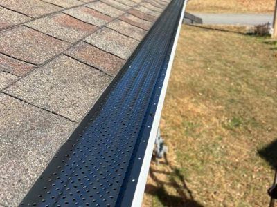 Black perforated gutter guard installed on a roof's edge.