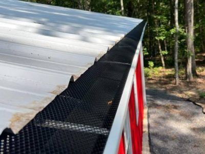 Black gutter guard on a red building with a white metal roof, trees in the background.