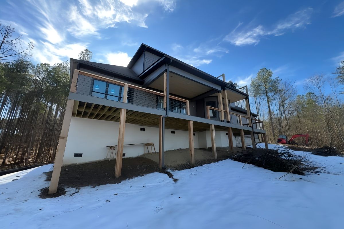 Modern two-story house with a gray facade, large deck, and a snowy yard under a blue sky.