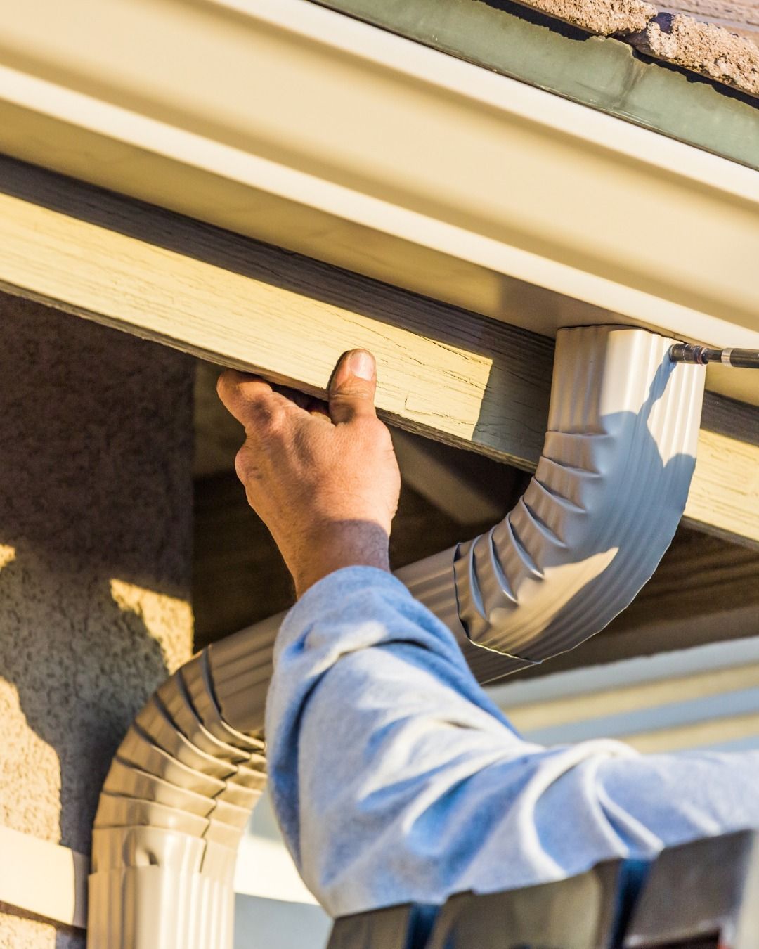 Person installing a beige gutter on a house.