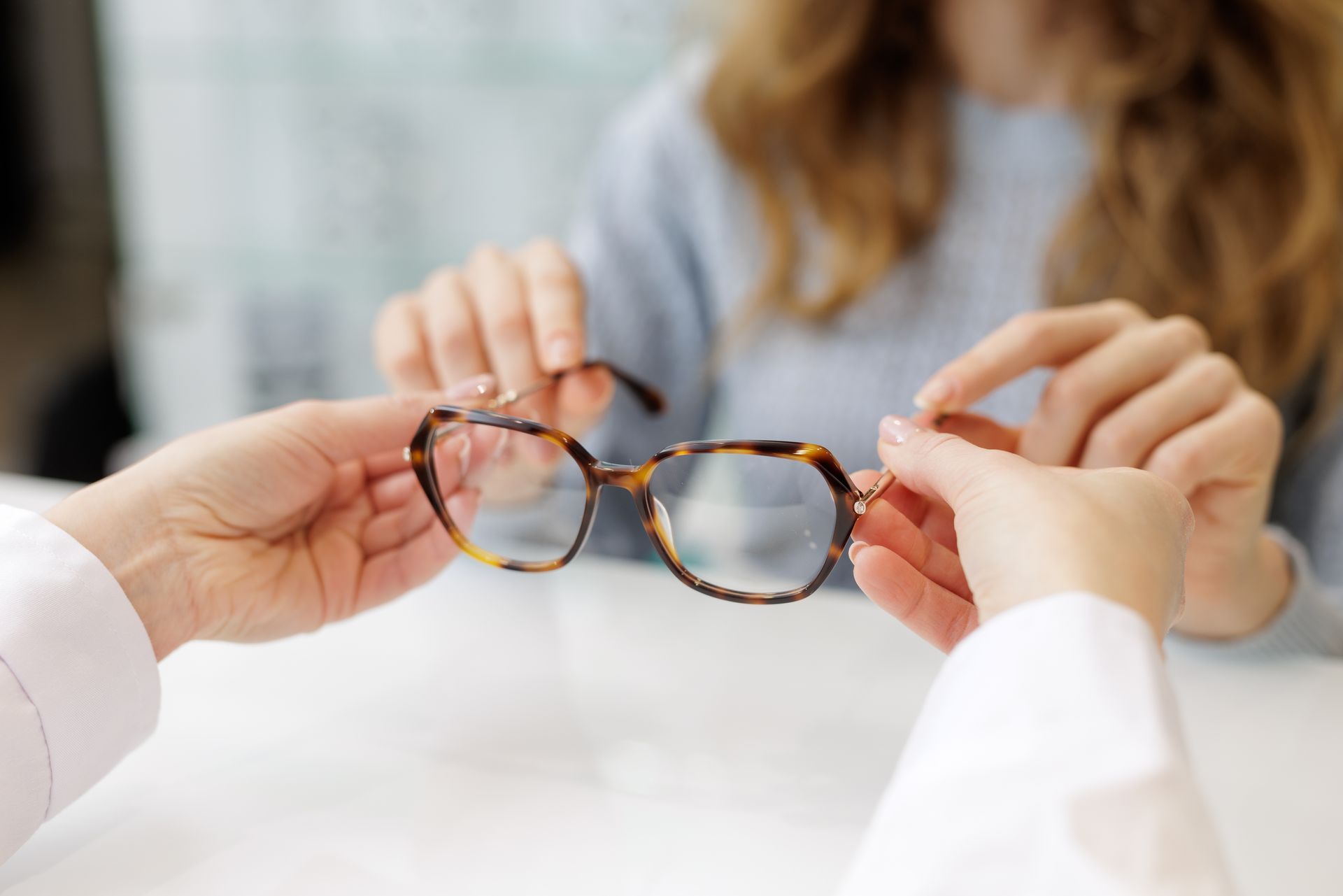 Hands holding tortoiseshell eyeglasses for adjustment during an eye exam