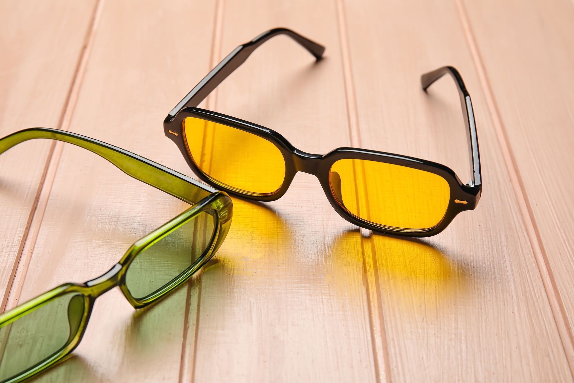 Yellow and green eyeglasses on a light wood surface