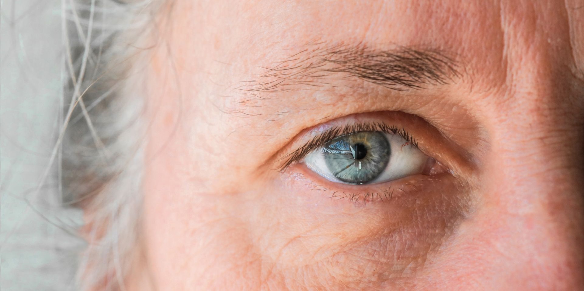 Close-up of a blue eye and surrounding skin with gray hair visible at the left edge