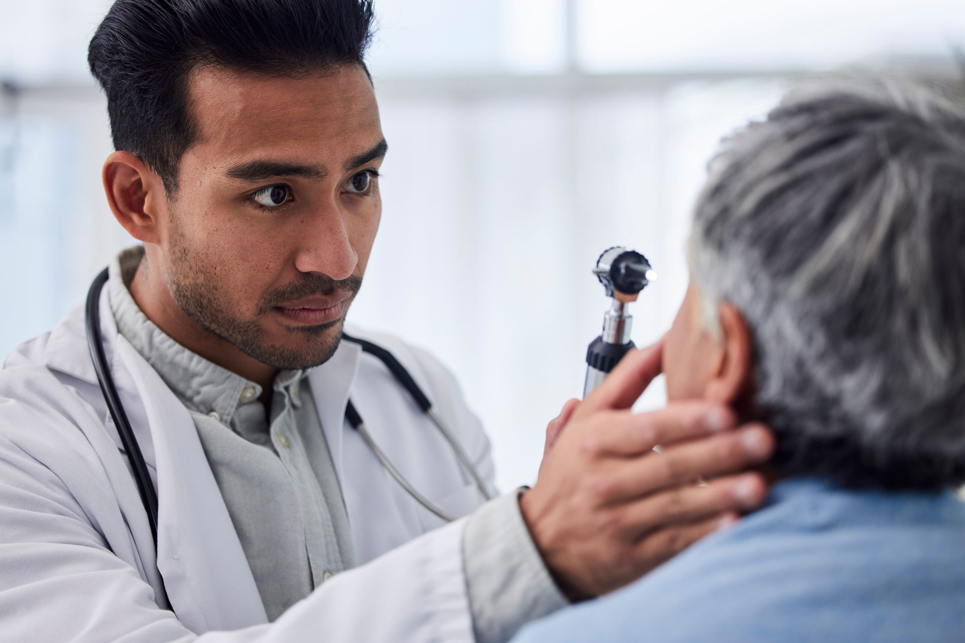 Doctor examining a patient’s eye with an otoscope in a clinic