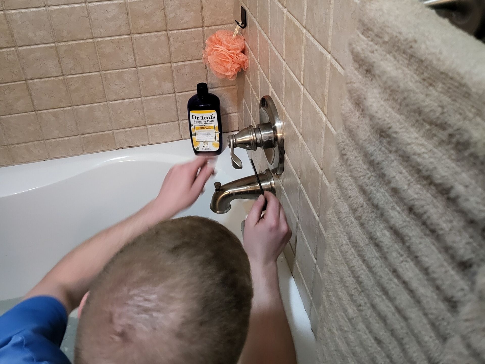 A man is fixing a bathtub faucet in a bathroom