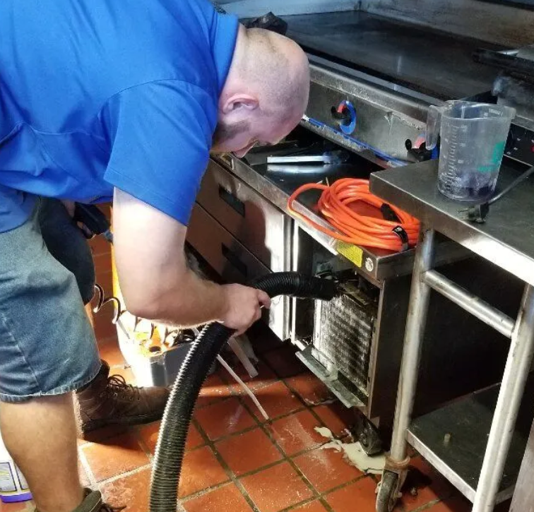 A man in a blue shirt is using a vacuum cleaner in a kitchen