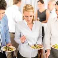 People serving plates of salad at a buffet table in a bright room