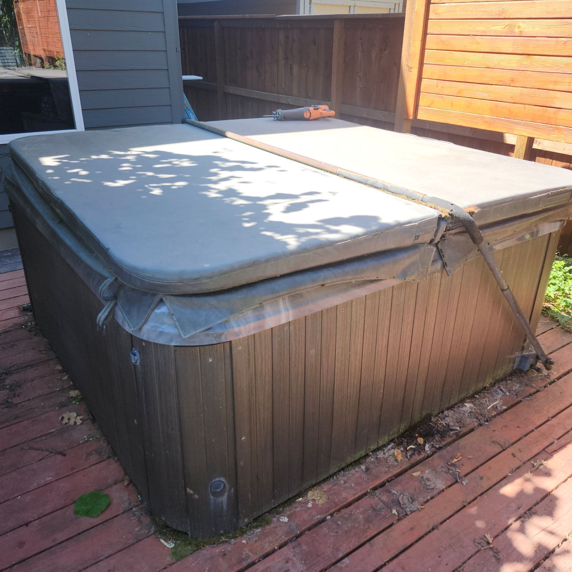 A brown hot tub with the cover on it sits on a wooden deck outdoors.
