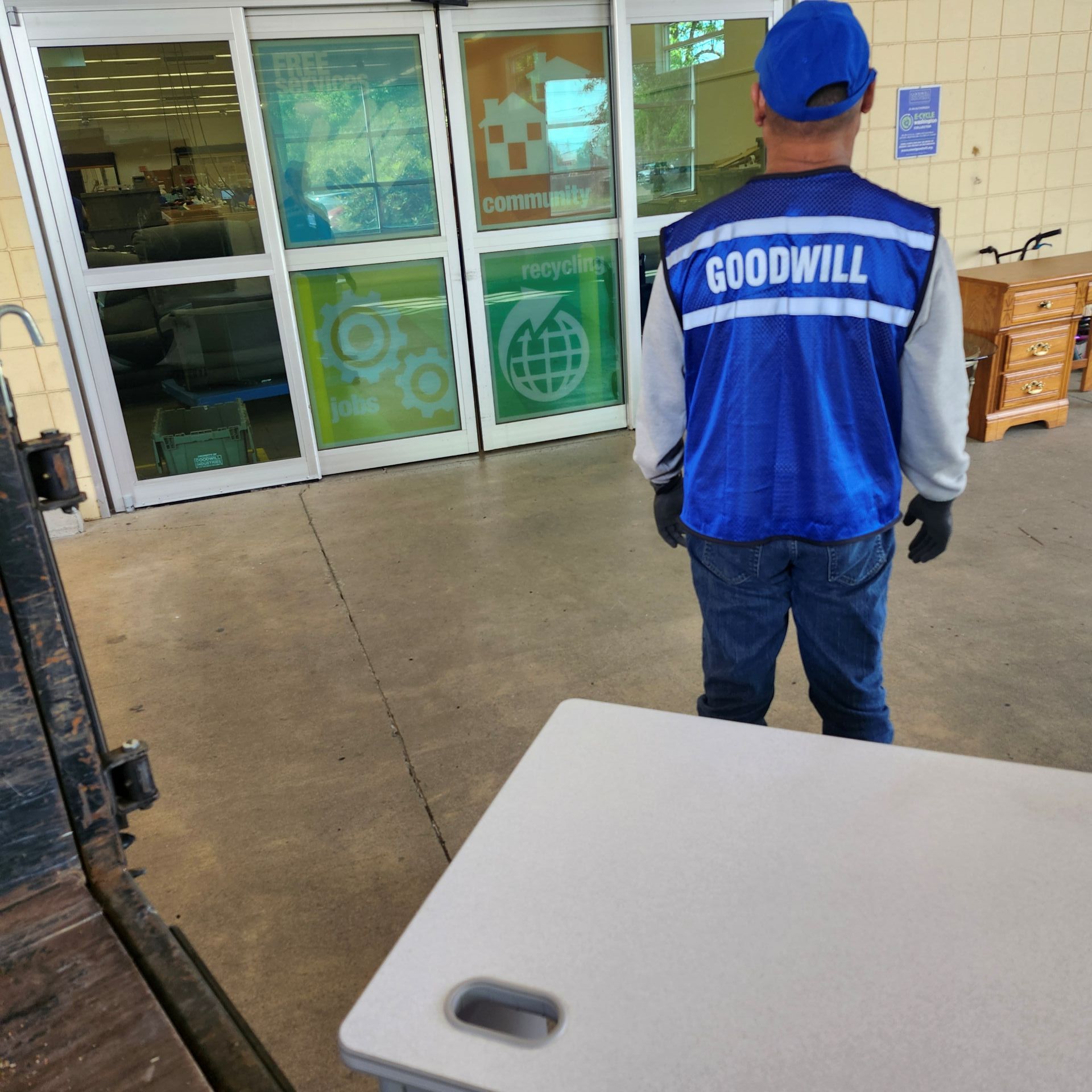 Person in blue Goodwill vest stands near entrance of Goodwill store.