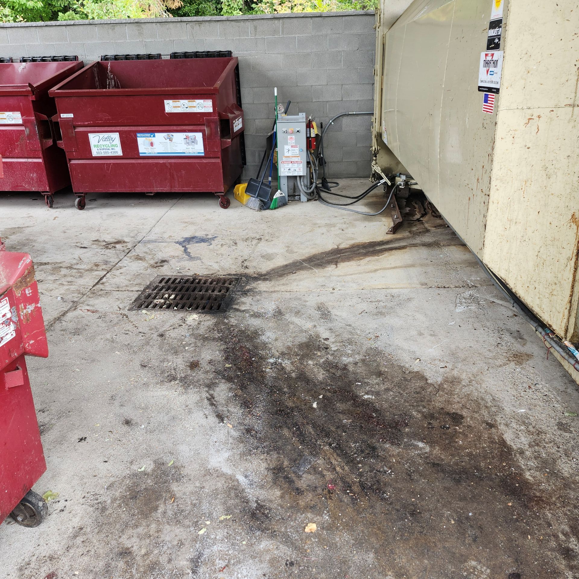 Dumpsters and trash stains on concrete by a drain.