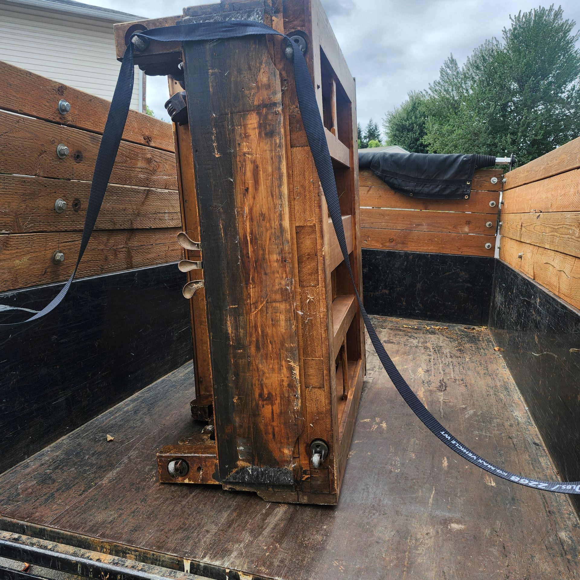 Wooden structure secured with straps inside a truck bed, likely for transport.