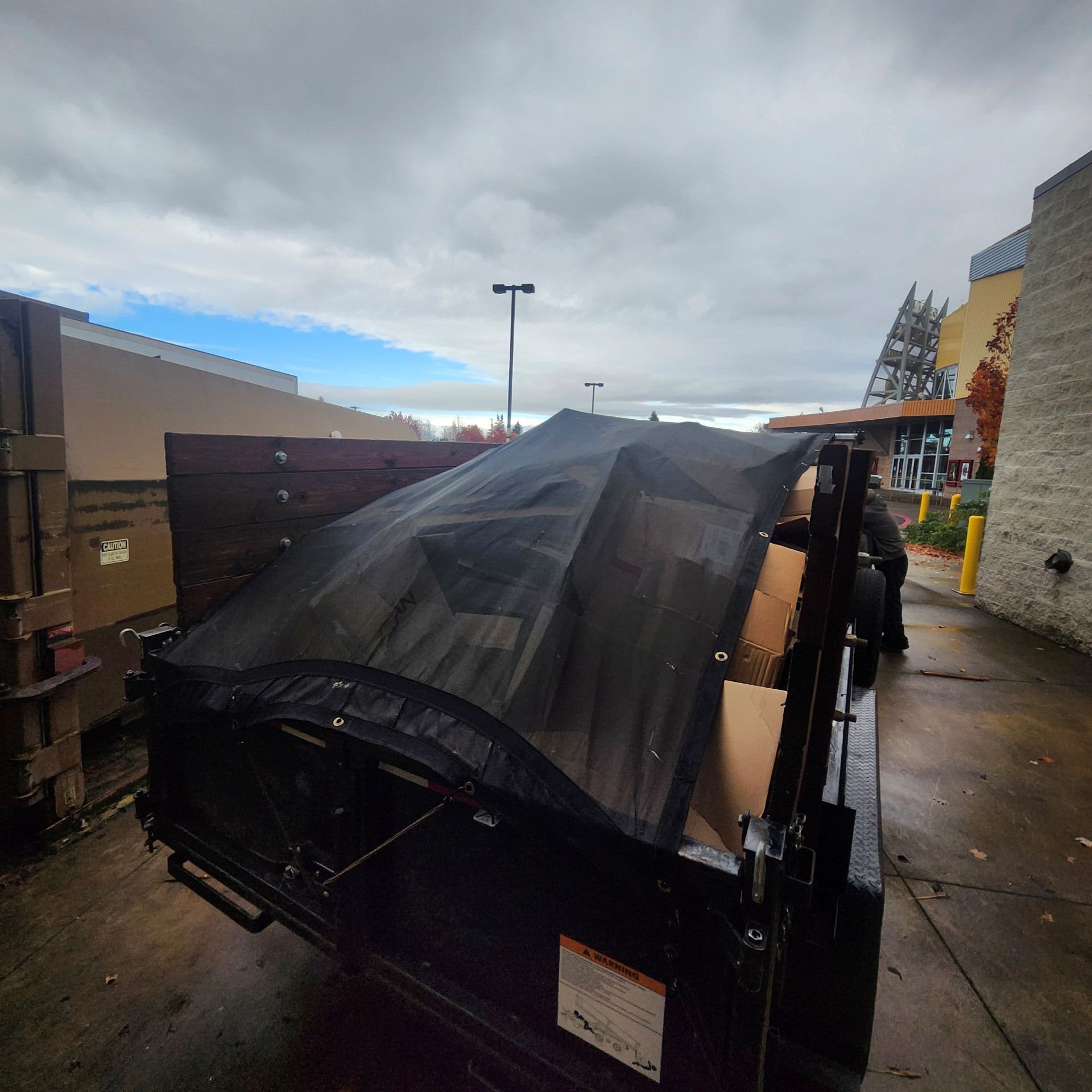 A black truck bed filled with boxes, covered by a black net, parked outside a building.