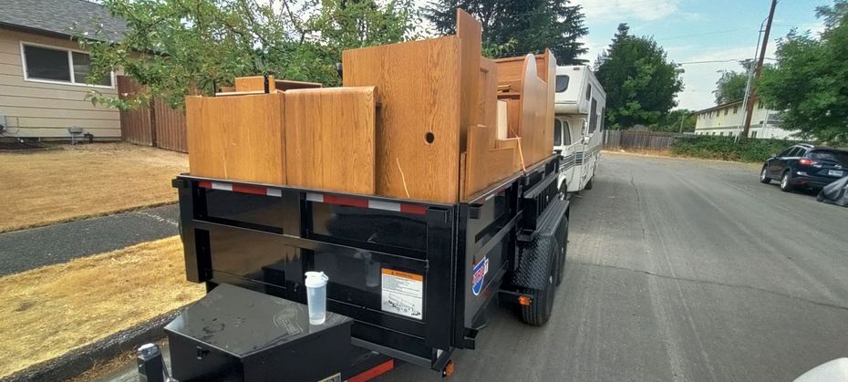 A truck with a trailer carrying wooden pieces parked on a paved road.